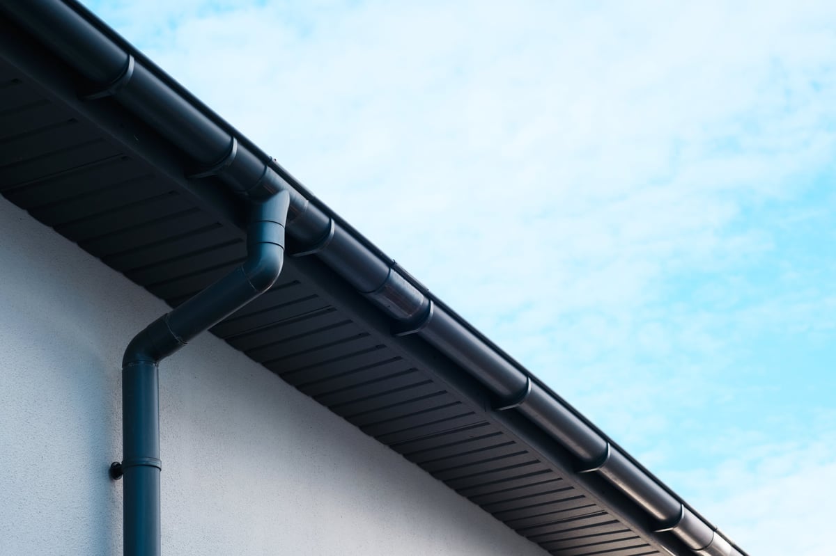 Sleek white gutter running along the roof edge with clouds above