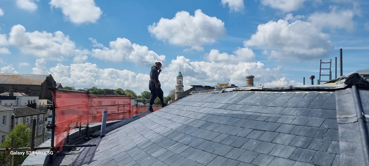 Worker standing on residential roof with slate tiles during daytime with blue sky and clouds