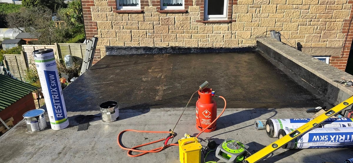 Worker in orange safety vest applying waterproofing sealant to a flat roof