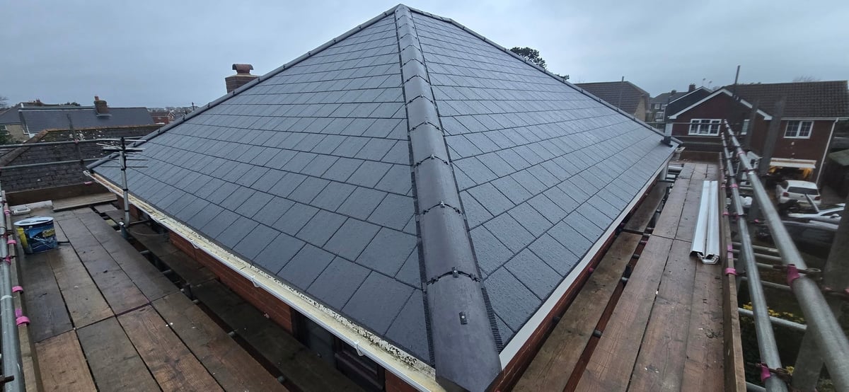 After — large modern building with pyramidal dark gray tiled roof and white trim, viewed from above