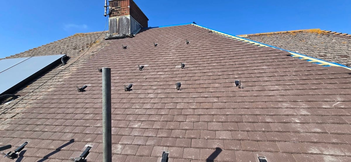 Residential roof with asphalt shingles, brick chimney, and metal ventilation pipe against clear blue sky